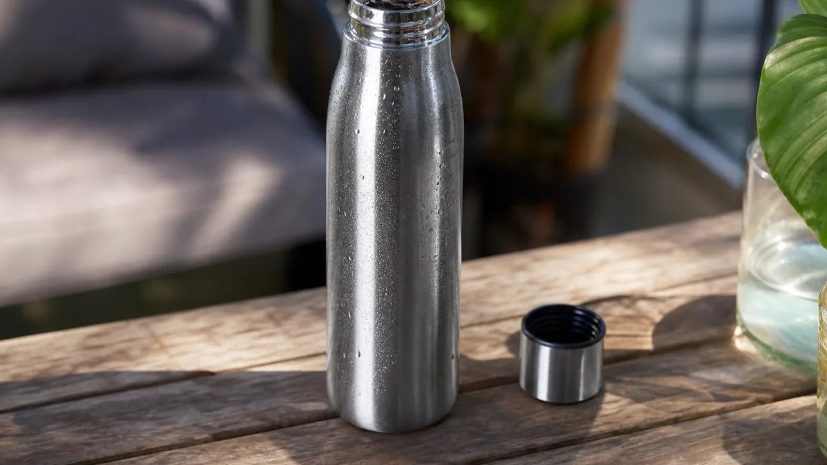 Bouteille isotherme en inox remplie d’eau pétillante fraîche, posée près de bulles et de glaçons