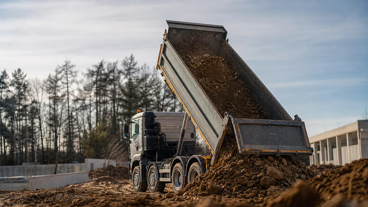 Camion benne chargé de terre quittant un chantier de terrassement avec une pelle hydraulique