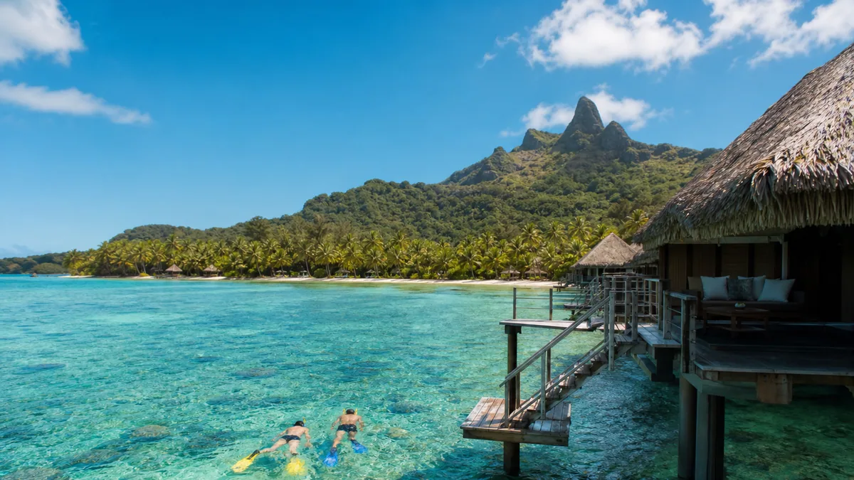 Bungalow sur pilotis au-dessus d’un lagon turquoise avec montagne tropicale en arrière-plan