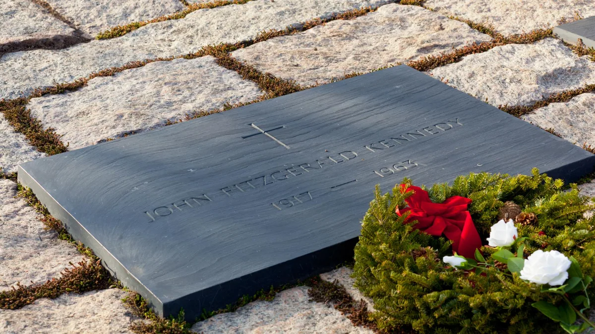 Plaque funéraire en granit gravée posée sur une sépulture fleurie dans un cimetière