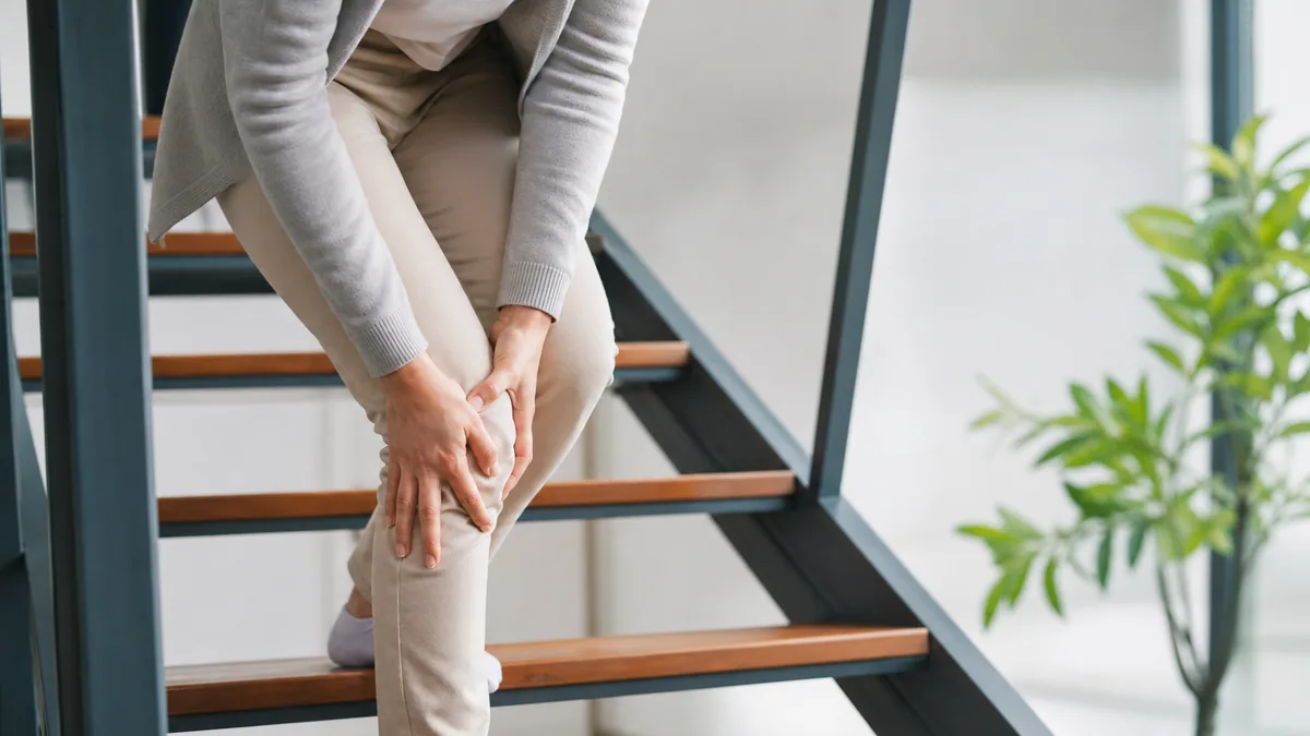 Personne descendant un escalier extérieur, main posée sur la rampe et sur le genou
