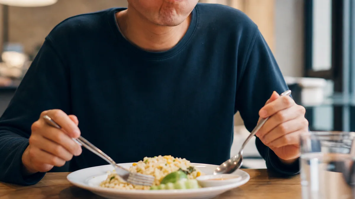 Personne attablée mangeant rapidement un plat avec fourchette et cuillère