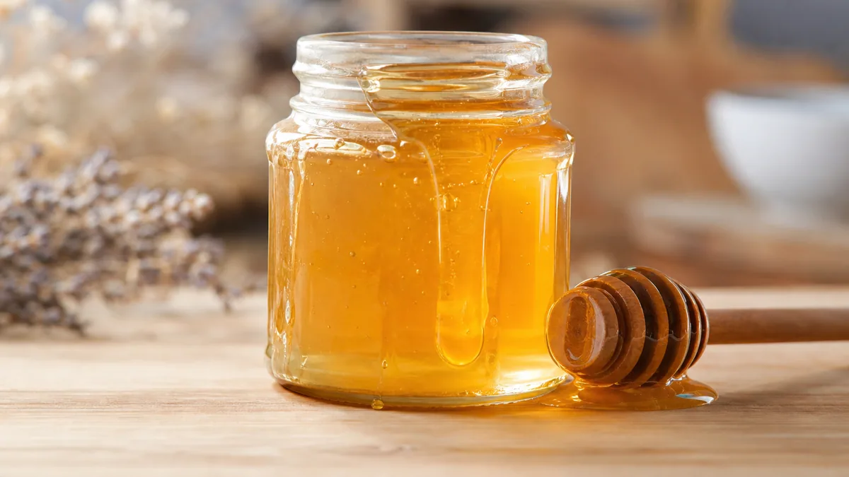 Pot de miel ouvert avec du miel doré et un miel-dipper posés sur une table en bois