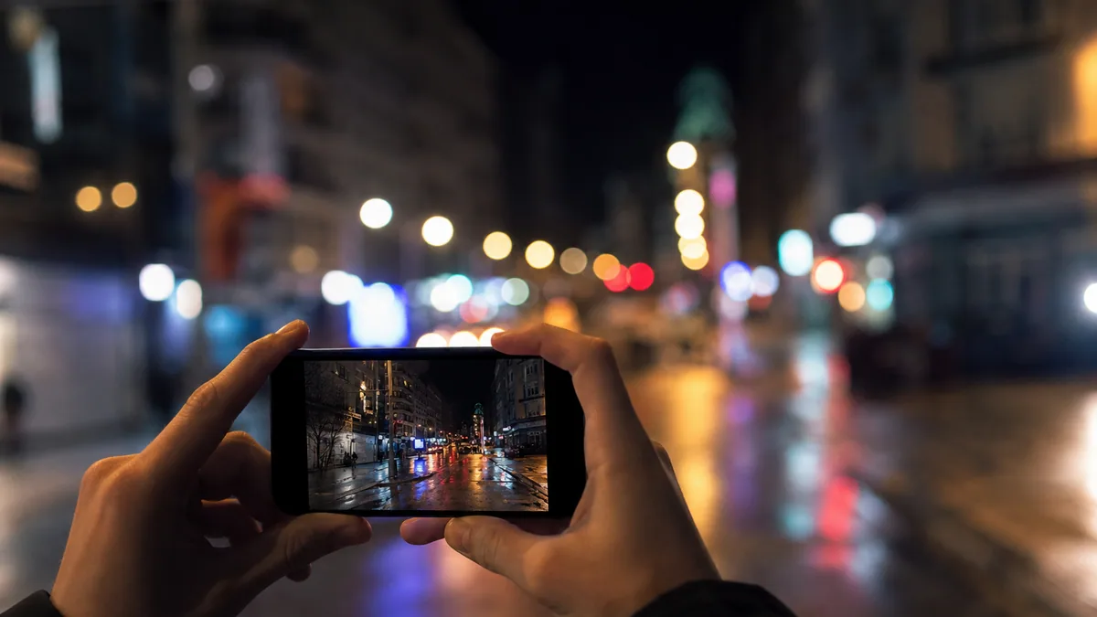 Smartphone tenu à deux mains photographiant une scène urbaine de nuit avec des lumières floues