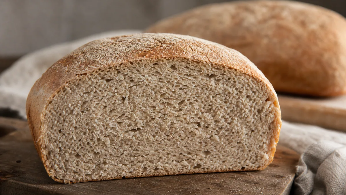 Pain maison tranché sur une planche en bois, mie serrée visible et farine saupoudrée