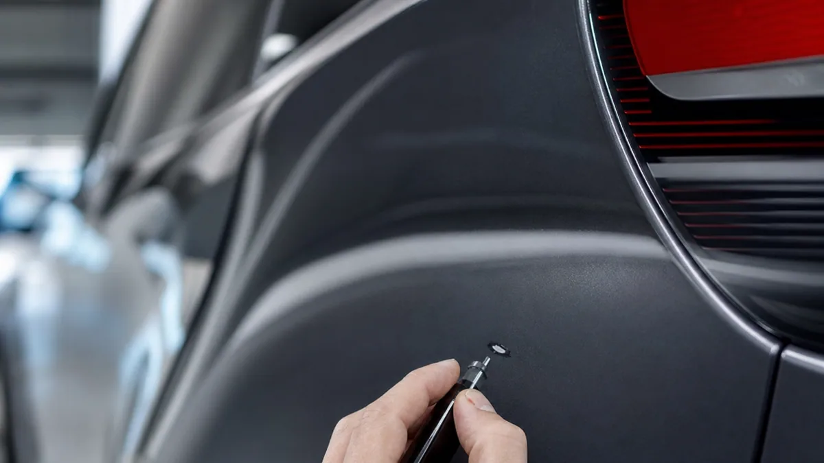 Gros plan d’une Tesla Model Y blanche avec un stylo de retouche près d’un éclat de peinture sur le capot